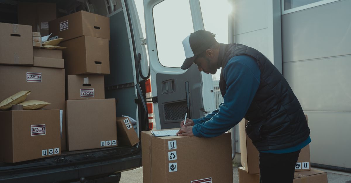 Delivery worker sorting and organizing cardboard boxes in van for shipment.