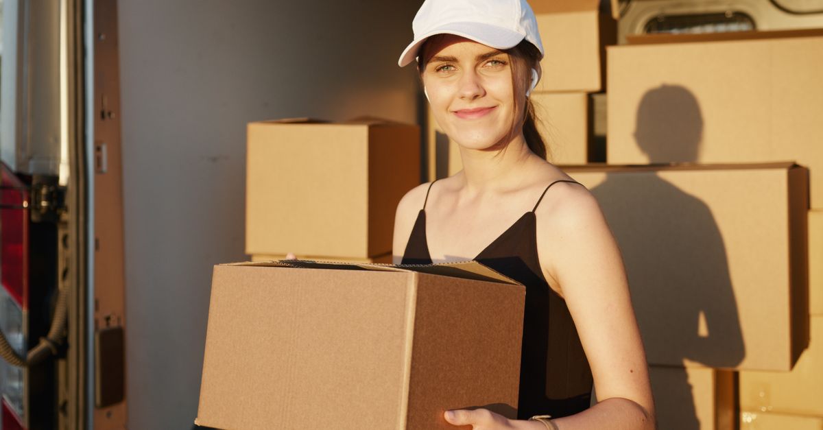 A cheerful female courier holds a cardboard box, symbolizing fast delivery service.