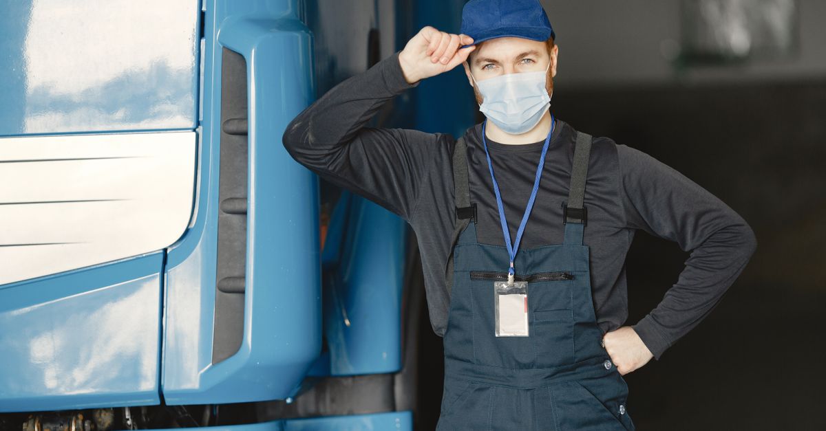 Mechanic in overalls and mask by blue truck in garage setting.